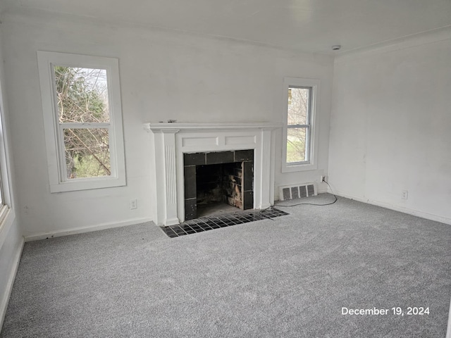 unfurnished living room with dark colored carpet, crown molding, and a tile fireplace