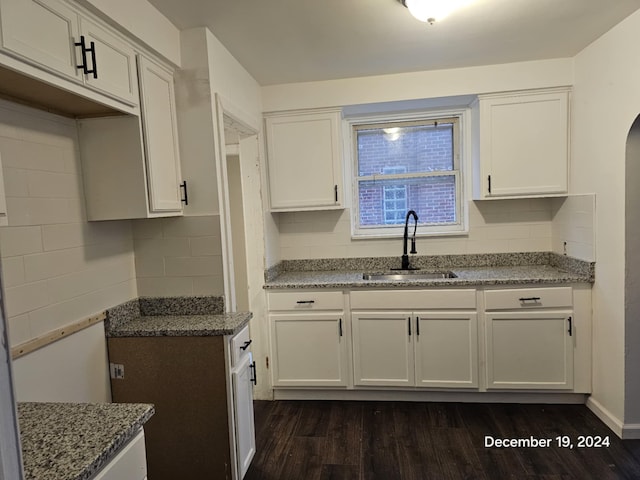 kitchen with backsplash, light stone counters, sink, dark hardwood / wood-style floors, and white cabinetry