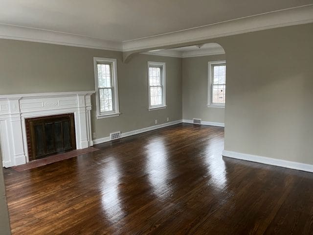 unfurnished living room with a healthy amount of sunlight, crown molding, and dark wood-type flooring