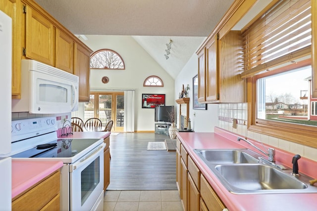 kitchen featuring white appliances, sink, vaulted ceiling, light tile patterned floors, and a textured ceiling