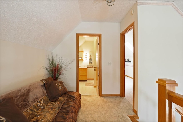 hall with a textured ceiling, light carpet, and vaulted ceiling