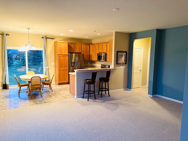 kitchen with hanging light fixtures, stainless steel appliances, kitchen peninsula, light carpet, and a breakfast bar