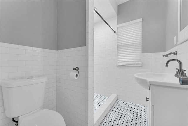 bathroom featuring vanity, toilet, tile walls, and a tile shower