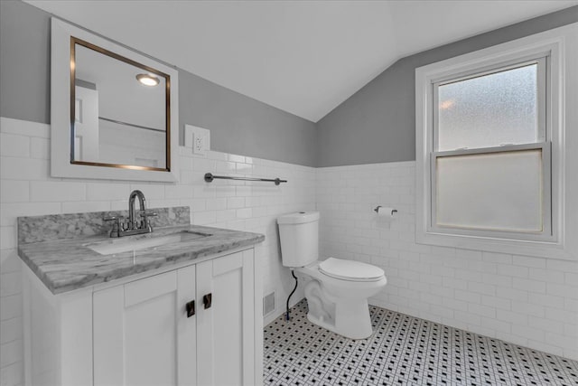 bathroom featuring tile walls, vanity, vaulted ceiling, and toilet