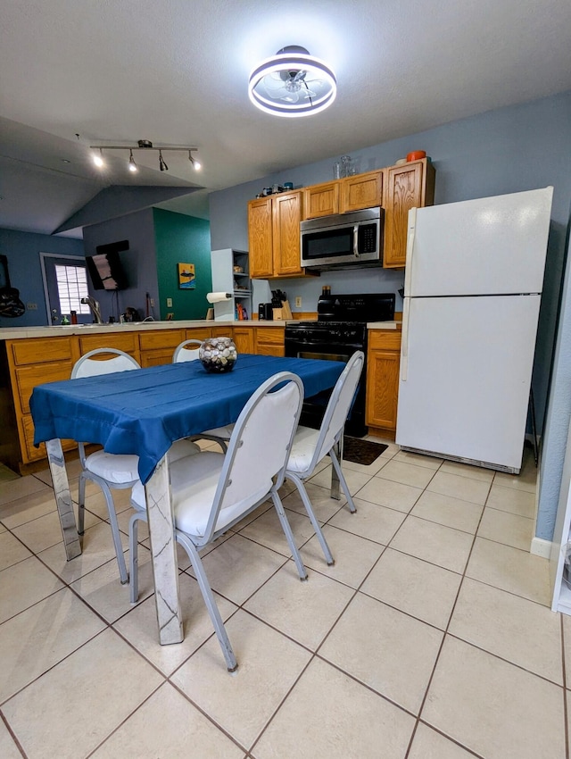 kitchen with white fridge, black range, lofted ceiling, and light tile patterned flooring