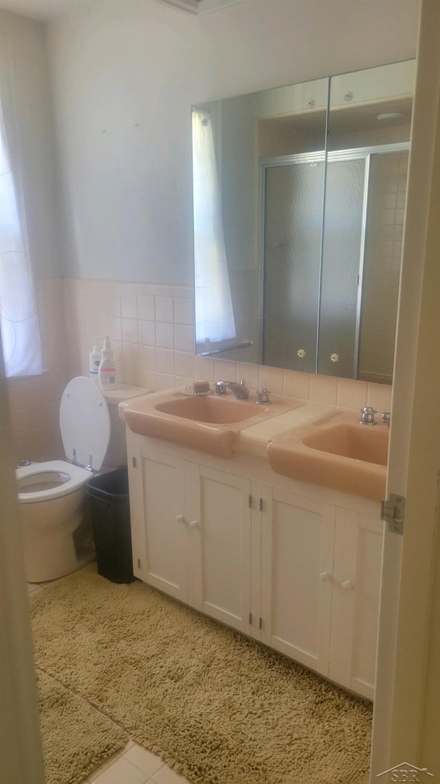 bathroom with tile patterned flooring, toilet, vanity, a shower with shower door, and tile walls