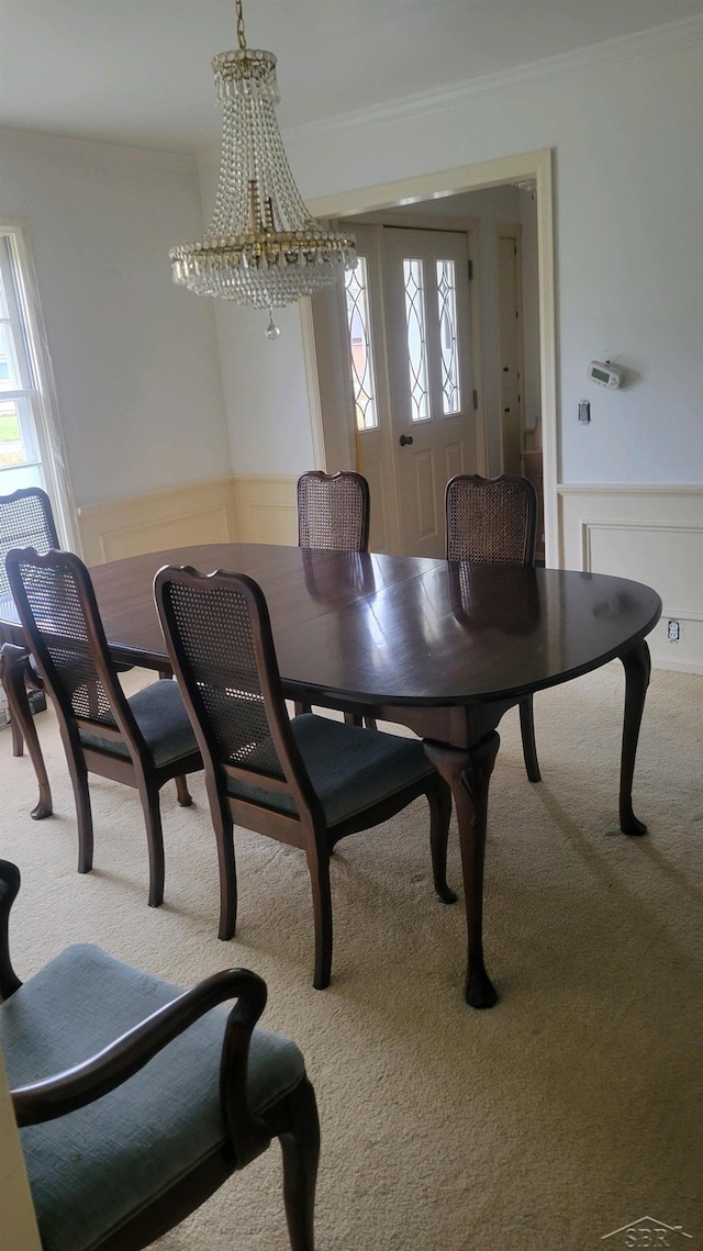 carpeted dining room with crown molding and an inviting chandelier