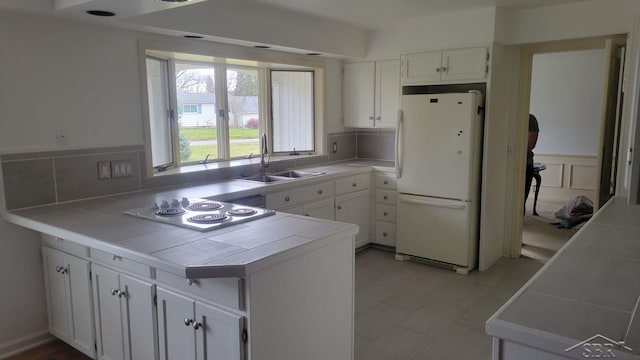 kitchen with white refrigerator, tile countertops, white cabinetry, and sink