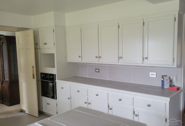 kitchen featuring tasteful backsplash, black oven, white cabinetry, and tile counters