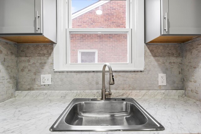 kitchen with gray cabinetry, backsplash, light stone counters, and sink