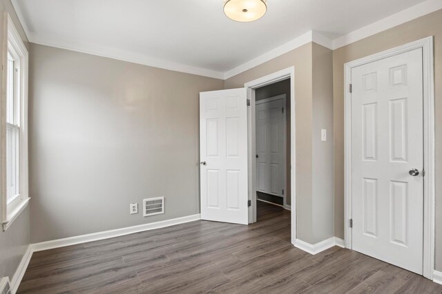 unfurnished bedroom with a closet, dark hardwood / wood-style floors, and ornamental molding