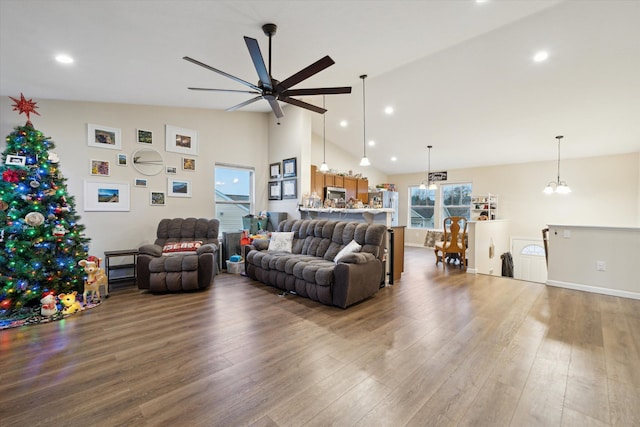 living room featuring ceiling fan with notable chandelier, wood-type flooring, and vaulted ceiling