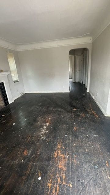 unfurnished living room featuring a tiled fireplace, crown molding, and dark wood-type flooring