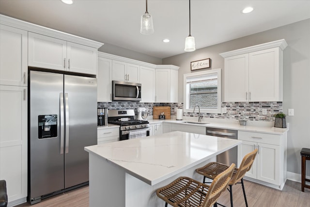 kitchen featuring appliances with stainless steel finishes, sink, decorative light fixtures, white cabinets, and light hardwood / wood-style floors