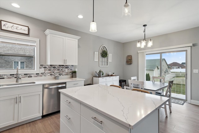 kitchen with a center island, sink, hanging light fixtures, stainless steel dishwasher, and white cabinetry