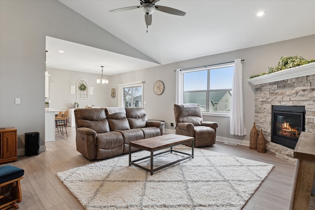 living room featuring ceiling fan with notable chandelier, light wood-type flooring, a fireplace, and vaulted ceiling