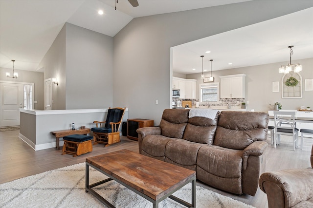 living room with ceiling fan with notable chandelier, wood-type flooring, and lofted ceiling