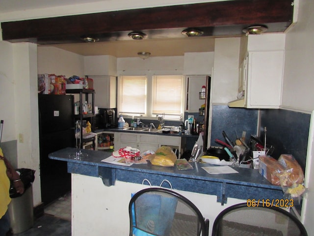 kitchen with white cabinetry, black fridge, and sink