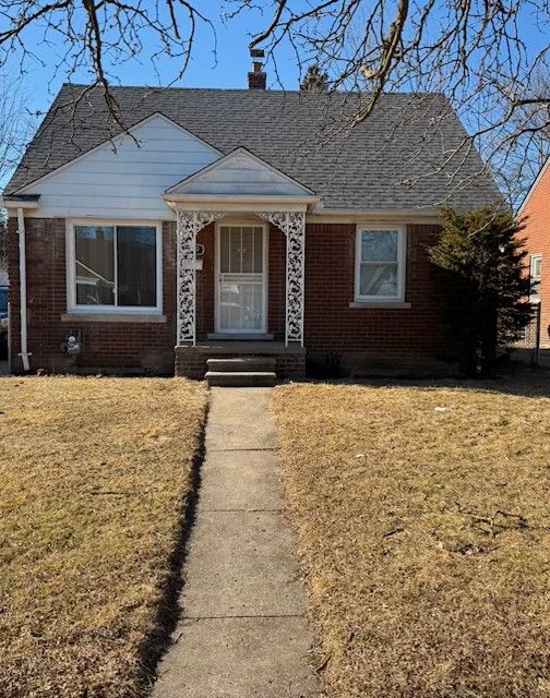 bungalow-style home featuring brick siding, a chimney, a front lawn, and roof with shingles