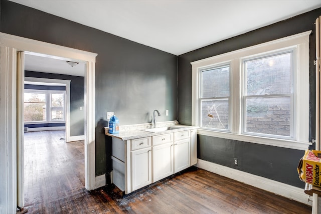 kitchen with light stone countertops, dark hardwood / wood-style flooring, white cabinetry, and sink