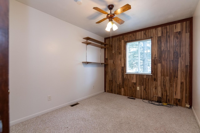 unfurnished room featuring light colored carpet, ceiling fan, and wooden walls