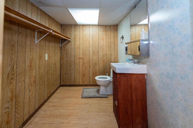 bathroom featuring vanity, a drop ceiling, wood-type flooring, and wooden walls