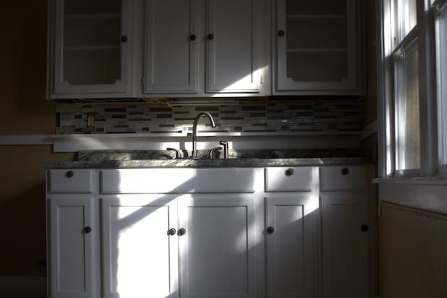 kitchen with backsplash, white cabinetry, and sink