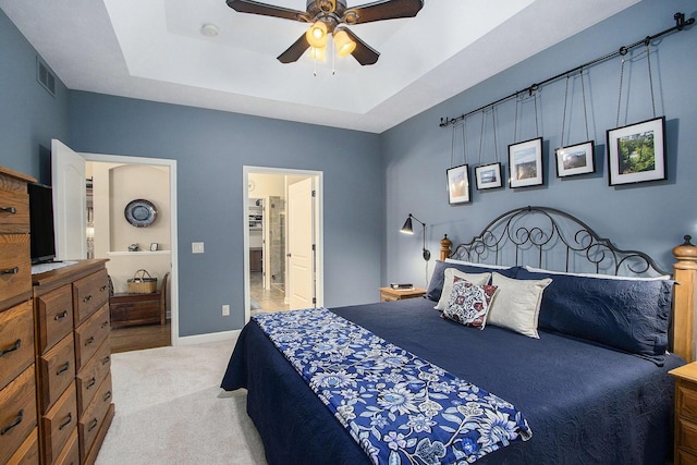 bedroom with connected bathroom, a tray ceiling, ceiling fan, and light colored carpet