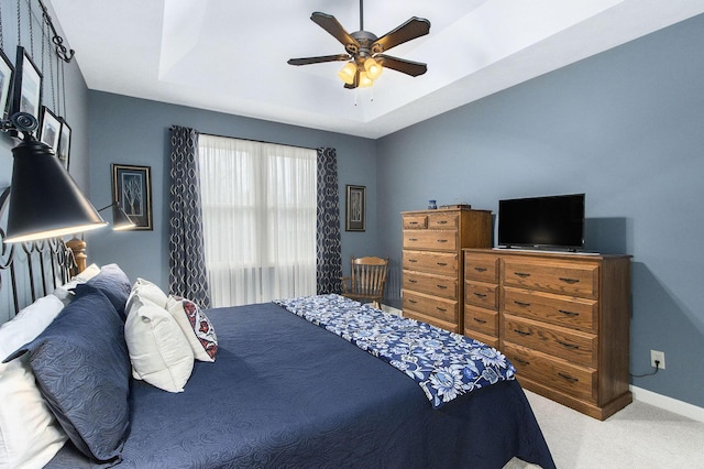 bedroom with ceiling fan, light carpet, and a tray ceiling