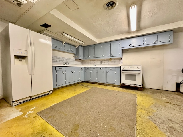 kitchen with decorative backsplash, range, white fridge with ice dispenser, and gray cabinetry