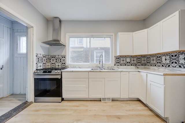 kitchen featuring stainless steel range, white cabinetry, wall chimney exhaust hood, and sink