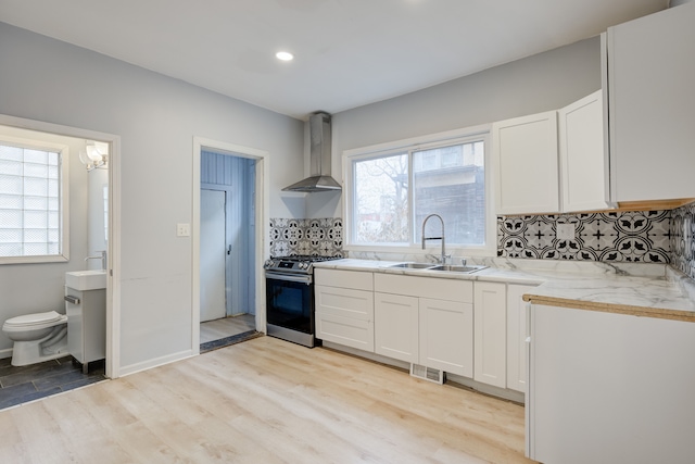 kitchen with wall chimney exhaust hood, white cabinets, stainless steel stove, and decorative backsplash