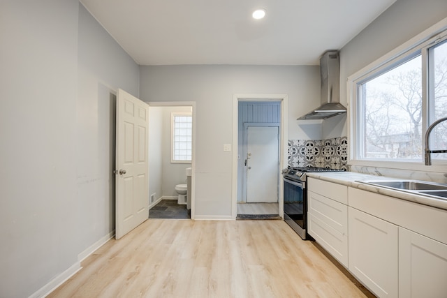 kitchen featuring gas stove, white cabinetry, sink, wall chimney exhaust hood, and light hardwood / wood-style floors