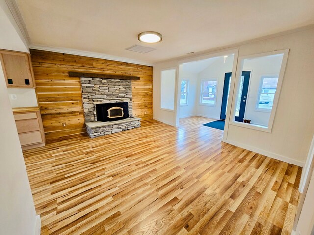 unfurnished living room with ornamental molding, a fireplace, wooden walls, and light hardwood / wood-style flooring