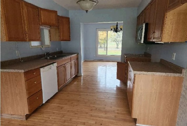 kitchen with white dishwasher, a notable chandelier, light wood-type flooring, and sink