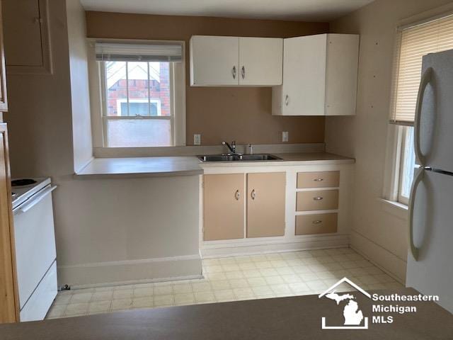 kitchen with white cabinets, stove, sink, and fridge