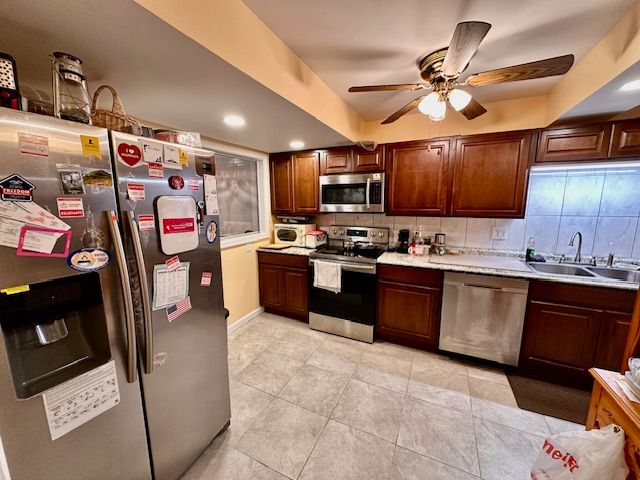 kitchen featuring ceiling fan, sink, decorative backsplash, light tile patterned floors, and appliances with stainless steel finishes