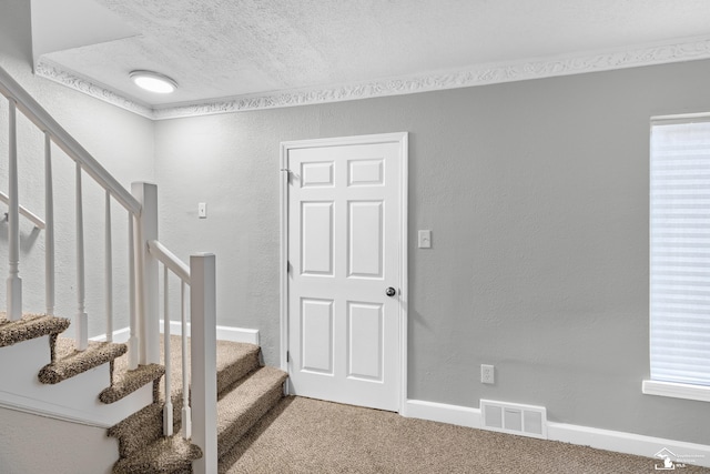 stairway featuring carpet, ornamental molding, and a textured ceiling