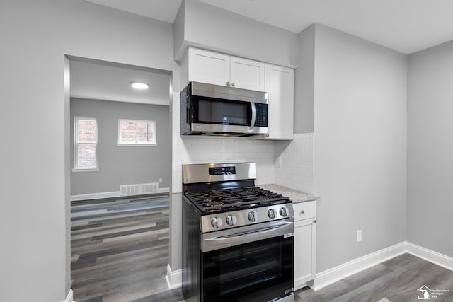 kitchen with white cabinets, decorative backsplash, stainless steel appliances, and hardwood / wood-style flooring