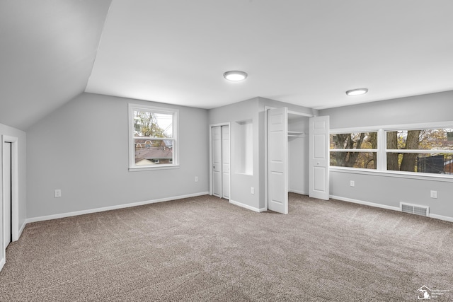 unfurnished bedroom featuring carpet flooring, two closets, and lofted ceiling