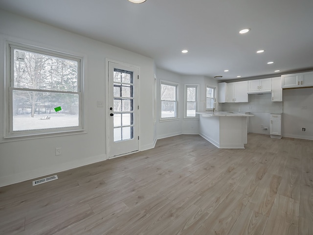 kitchen with sink, light hardwood / wood-style flooring, white cabinets, decorative backsplash, and kitchen peninsula