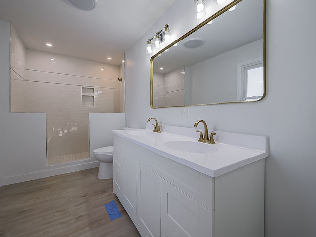 bathroom featuring vanity, tiled shower, hardwood / wood-style floors, and toilet