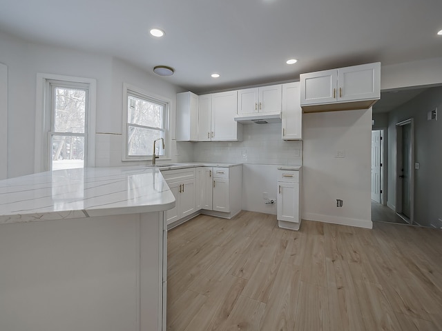 kitchen featuring sink, light hardwood / wood-style flooring, light stone countertops, decorative backsplash, and white cabinets