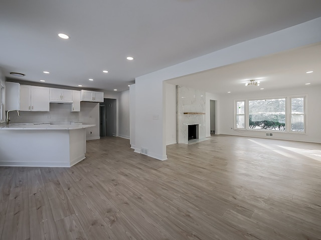 kitchen featuring tasteful backsplash, sink, white cabinets, a premium fireplace, and light wood-type flooring