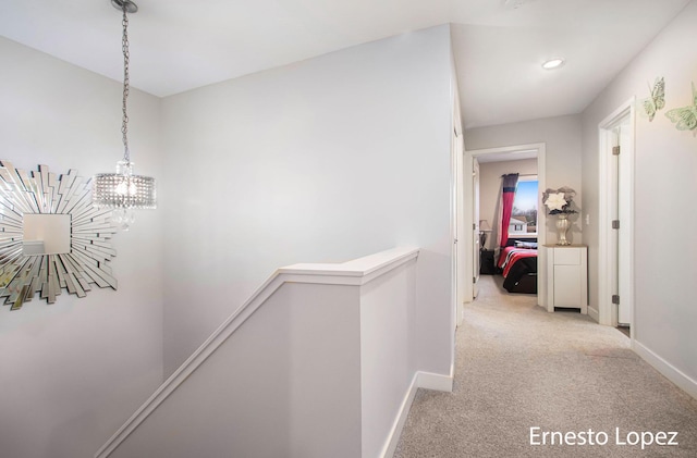 hall featuring light colored carpet and an inviting chandelier