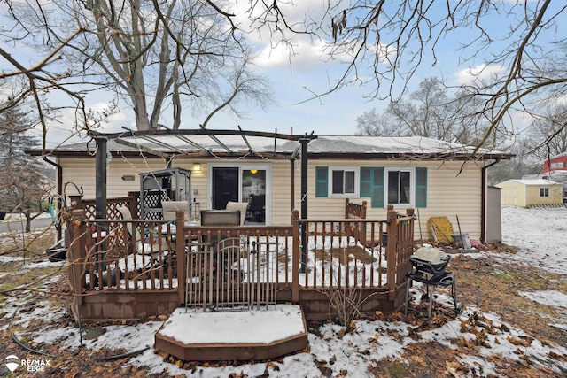 snow covered rear of property featuring a pergola, a storage shed, and a wooden deck