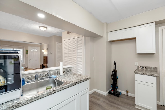 kitchen with white cabinets, light stone counters, sink, and light hardwood / wood-style flooring