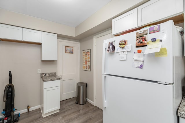 kitchen with white cabinets, white refrigerator, light stone counters, and light hardwood / wood-style floors