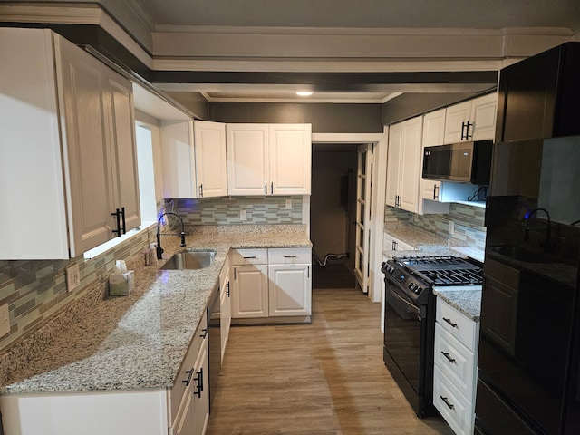 kitchen with light stone countertops, backsplash, black range with gas stovetop, sink, and white cabinets