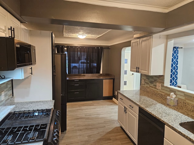 kitchen featuring tasteful backsplash, white cabinetry, light stone countertops, and black appliances